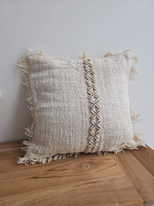 Coussin en tissu naturel avec franges et détails de coquillages, style bohème pour décoration intérieure.