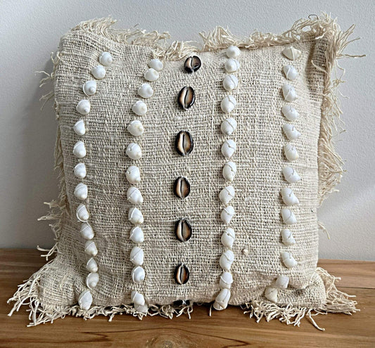 Coussin en tissu naturel orné de coquillages blancs et noirs, bordures frangées, style bohème.