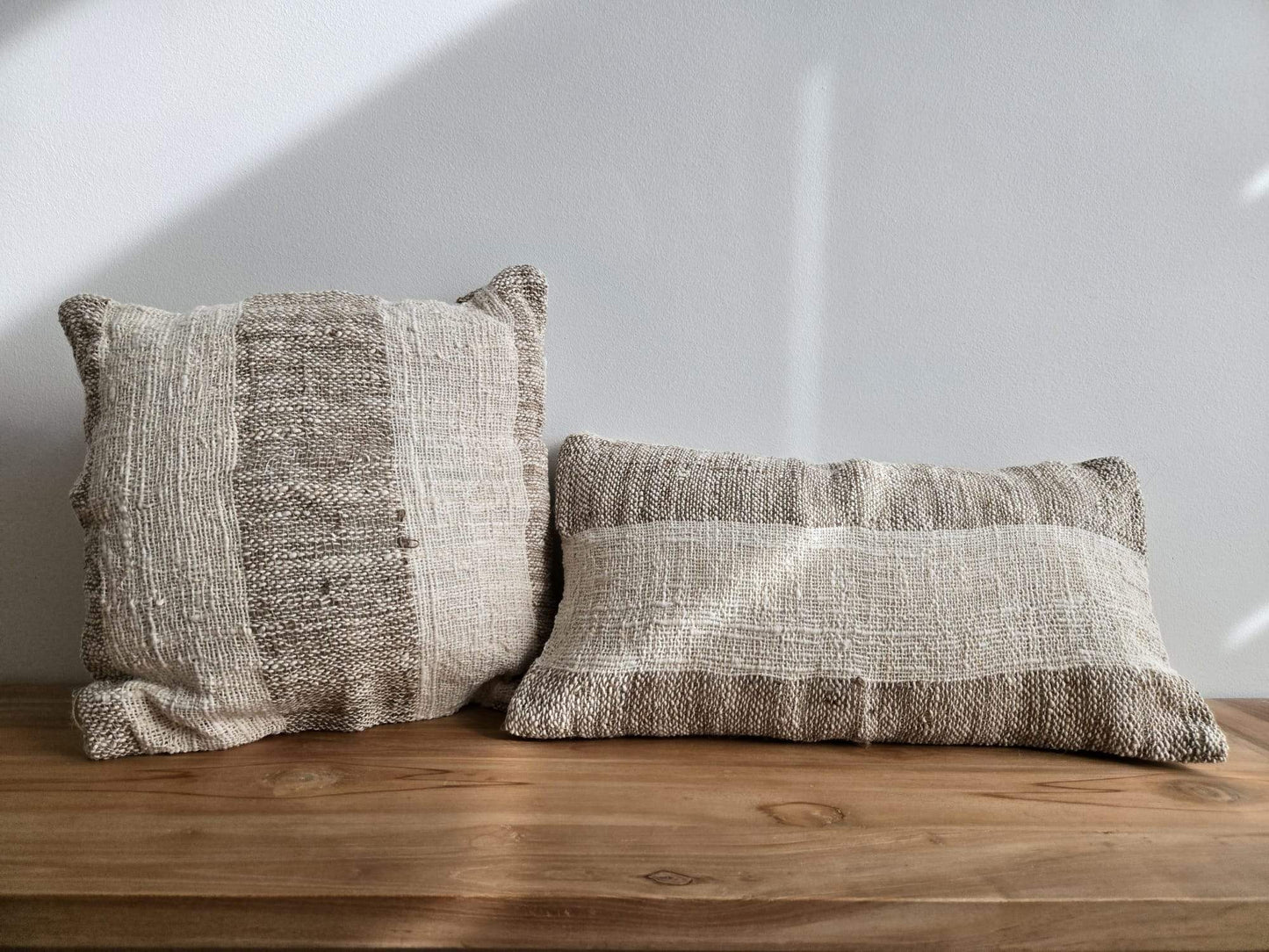 Deux coussins en tissu naturel texturé, posés sur une étagère en bois, pour une décoration intérieure chaleureuse.