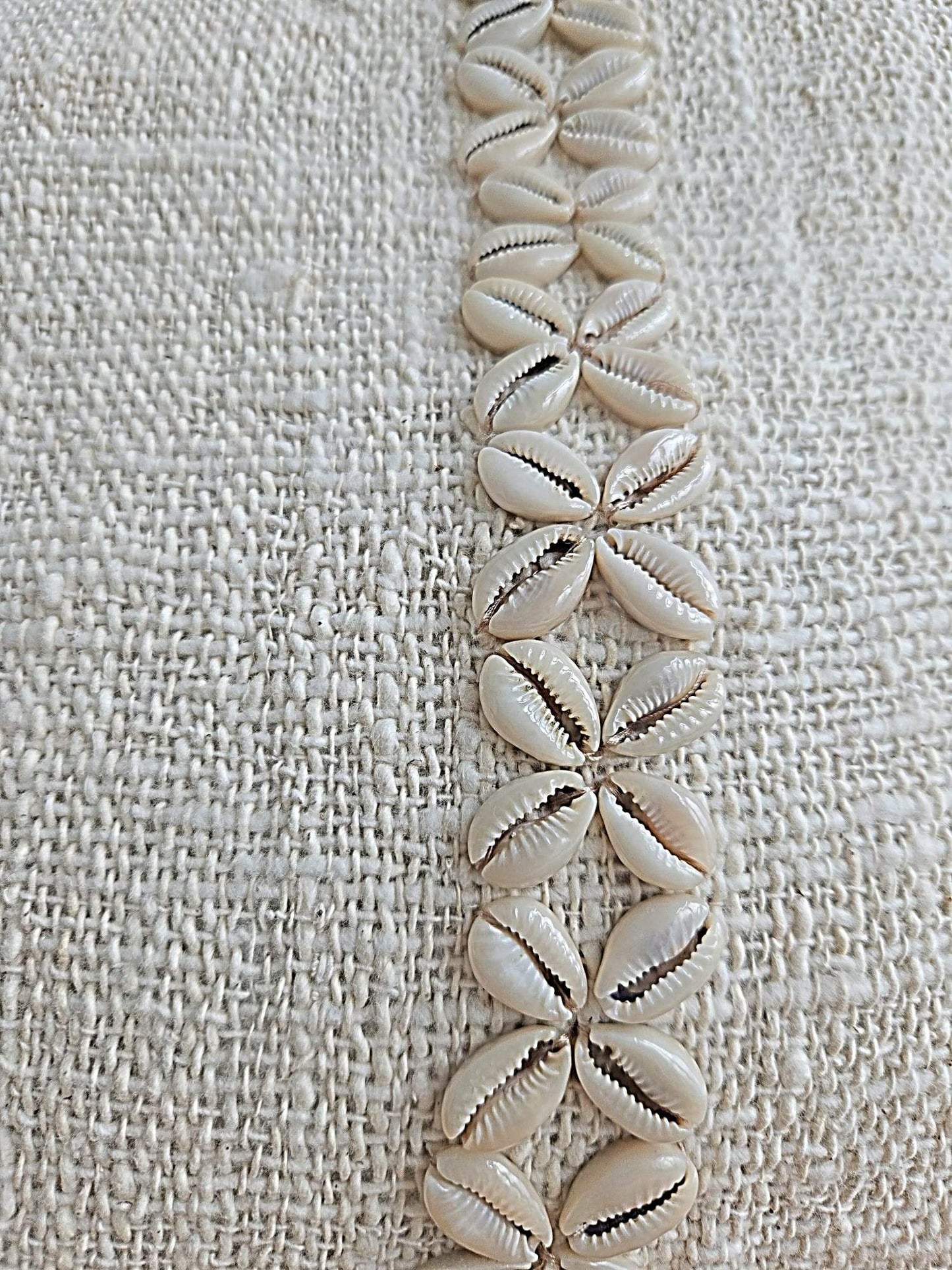 Coquillages naturels disposés en motif floral sur tissu texturé, décoration artisanale bohème.