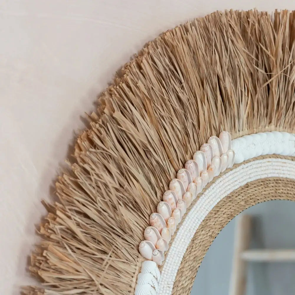 Miroir rond en rotin avec franges naturelles et coquillages, style bohème pour décoration intérieure.