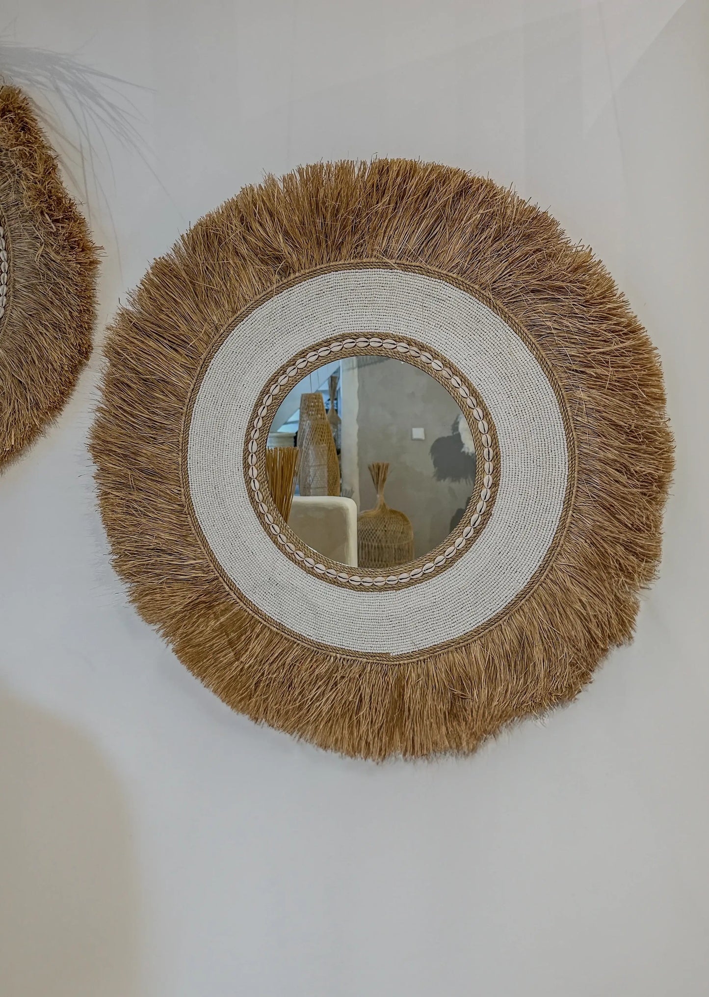Miroir rond en fibres naturelles avec bordure de coquillages, style bohème pour décoration intérieure.