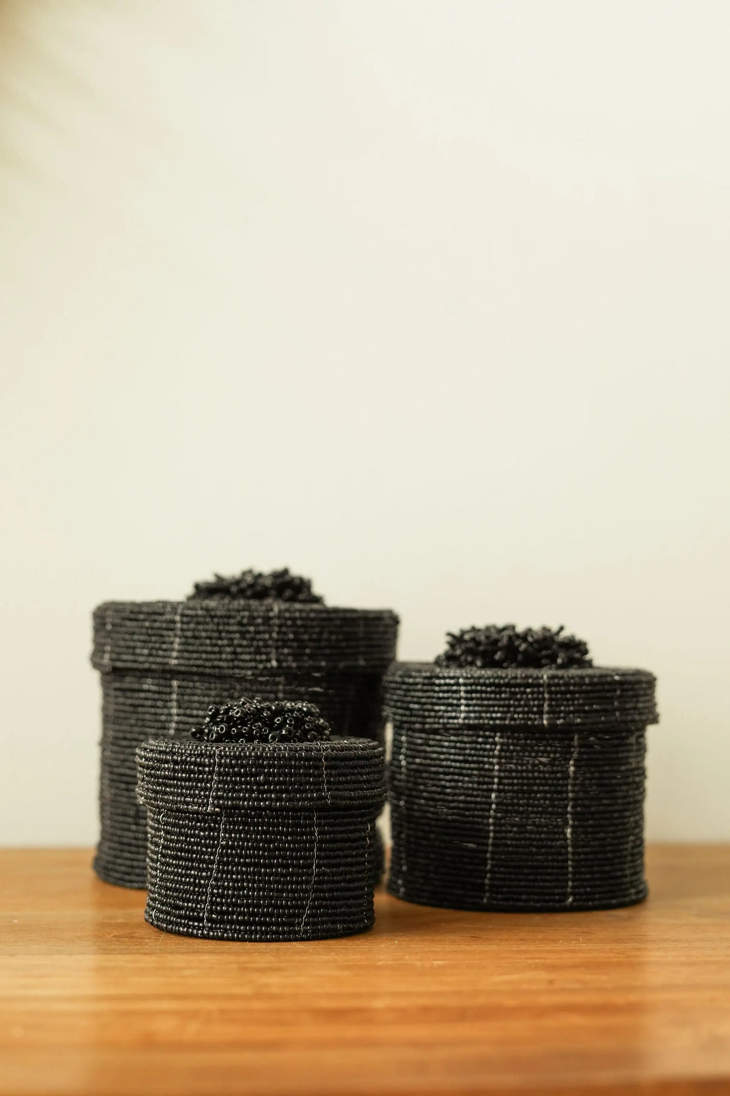 Trois paniers noirs tressés à la main, style bohème, posés sur une surface en bois.